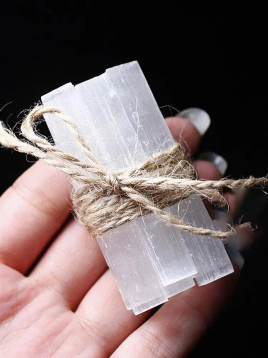 Selenite Rod Clear rectangular stones tied with twine on a hand against a dark background