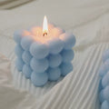 Bubble Cube Candle blue variant blowing GiftDealAU product image. Blue bubble-textured candle burning on a white fabric background