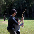 Burnt Boxed Wooden Boomerang through teaching kid GiftDealAU product image. Two people playing with a long stick in a grassy field with trees in the background