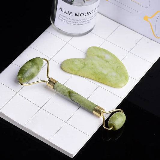 Facial Roller and Gua Sha Gift Set Green jade roller and gua sha tool on a white surface with a bottle of Blue Mountain coffee in the background.