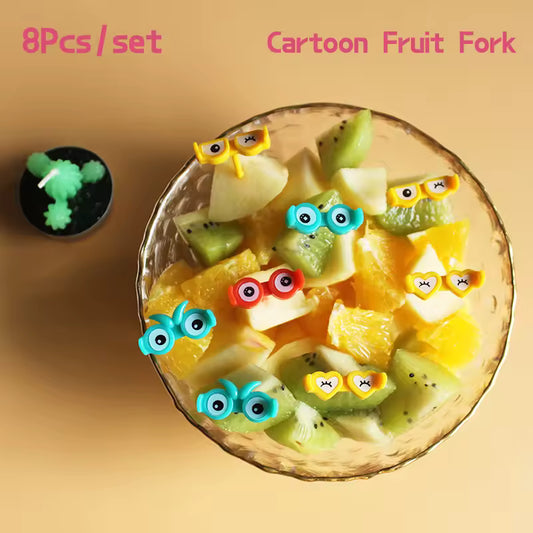 Goggles Food Pick Fruit skewers with cartoon fruit fork ends on a glass plate against a beige background.