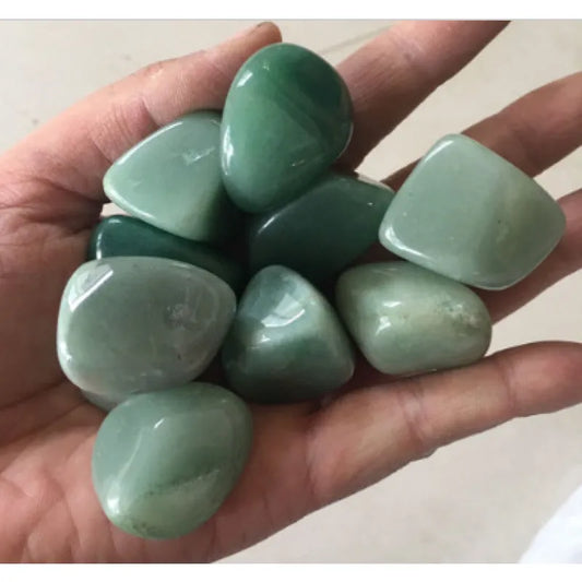 Green Aventurine Tumble Stones A hand holding a cluster of smooth, polished green tumbled stones, likely jadeite or nephrite chips, against a neutral light background.