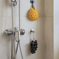 Handmade Grape Soap - Crystal Grape Soap bathroom uses image.
Shower head with a yellow sponge and black grapes hanging on hooks against a tiled wall.