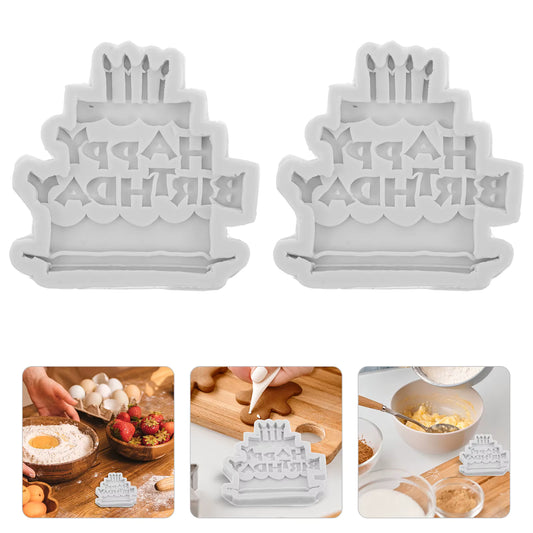 Happy Birthday Cake Silicone Mold Two white 'Happy Birthday' cake-shaped cookie cutters with baking ingredients and tools on a white background.
