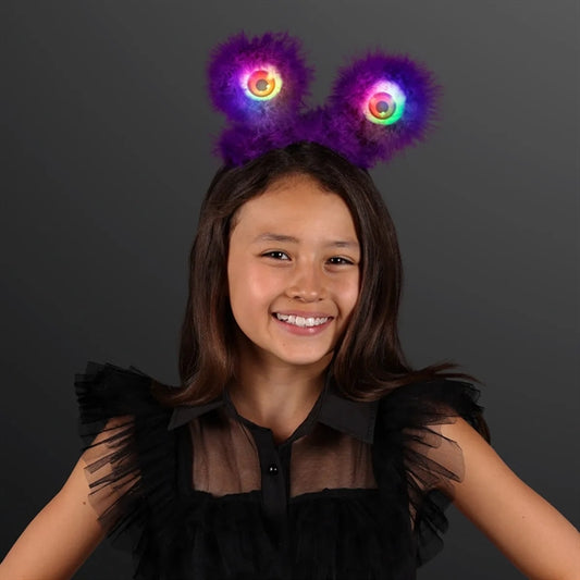 LED Wiggly Eye Head Boppers A smiling girl wearing a fuzzy purple headband with light-up, colorful eye-shaped details.