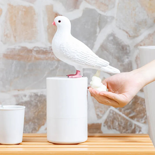 Pigeon Soap Dispenser White ceramic pigeon on a stand with a hand holding a bottle, against a marble background