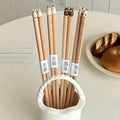 Plumpy Handmade Animal Chopsticks variant in basket GiftDealAU product image. Wooden chopsticks with animal-shaped tips in a white holder on a table with bread in the background.