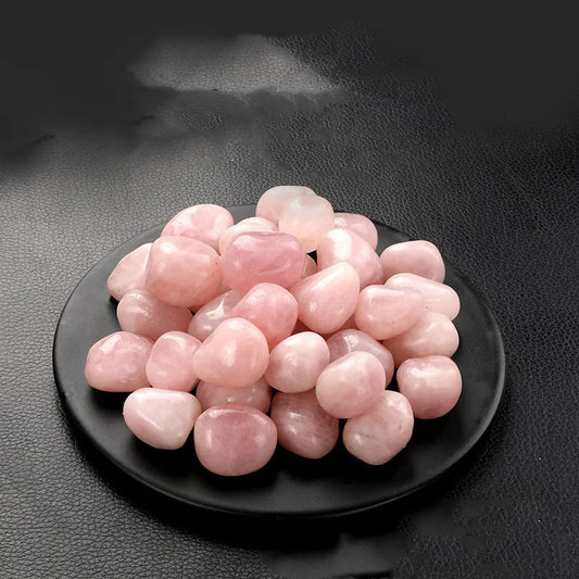 Rose Quartz Tumble Stone Pink stones on a black plate against a dark background
