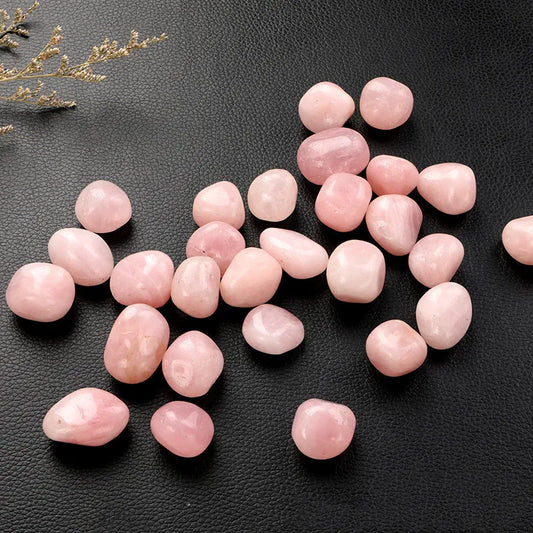 Rose Quartz Tumble Stone Pink stones on a black textured surface with decorative elements.