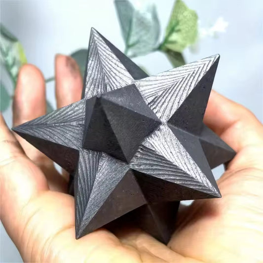 Shungite Merkaba Star Black geometric star-shaped object held in hands with a blurred natural background