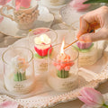 Tulip Bouquet Jar Candle Hand lighting a tulip-shaped candle on a decorative table with floral elements.