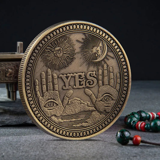 Yes No Boxed Divination Decision Coin A round bronze-toned metal coin or medallion with embossed sun, moon, eyes, and the word “YES,” photographed on a dark gray surface with a blurred decorative object and beads in the background.